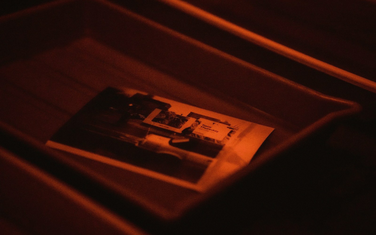 A developing tray under safelight, print emerging