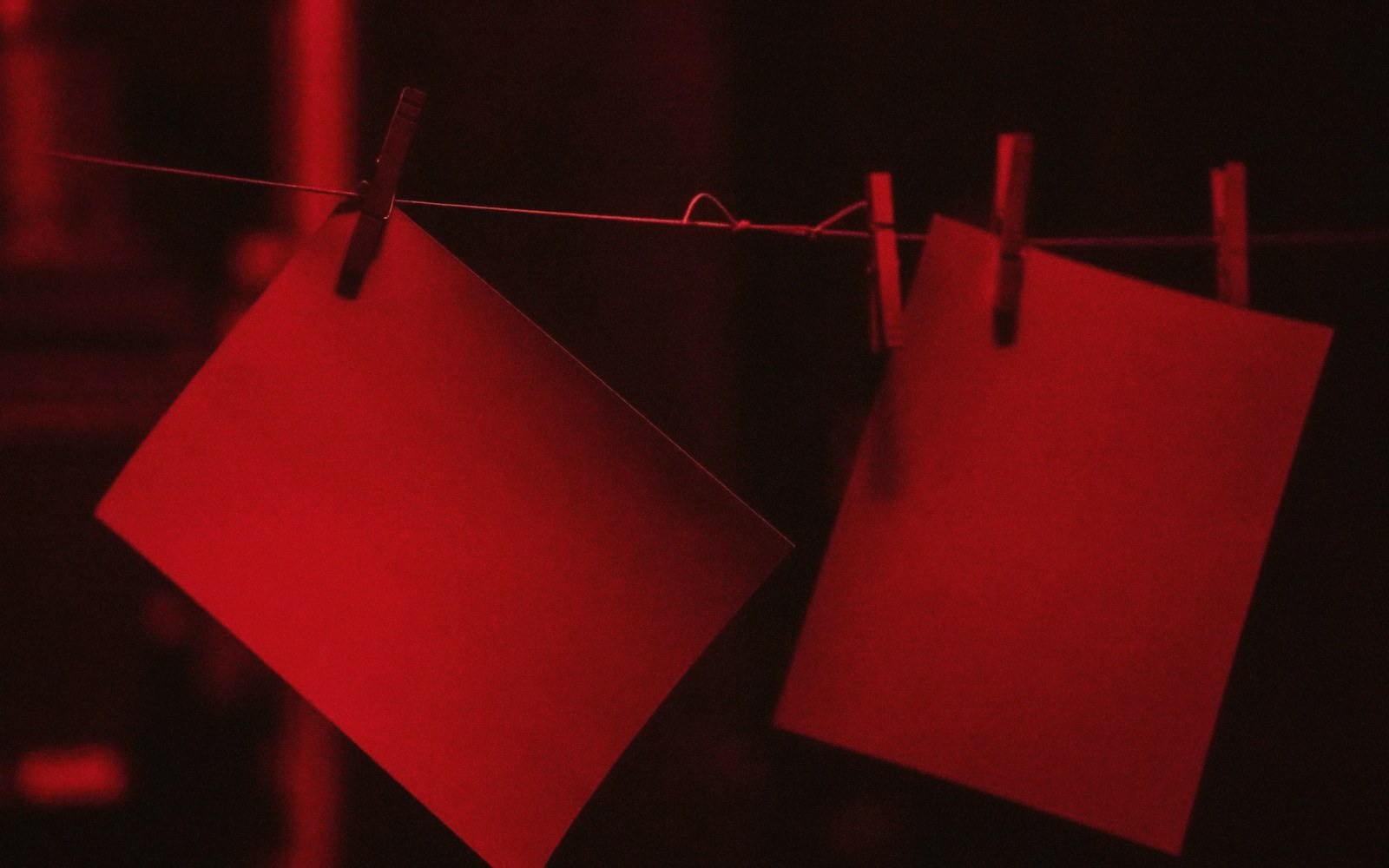 Blank sheets of paper hang from clothespins on a wire under red light