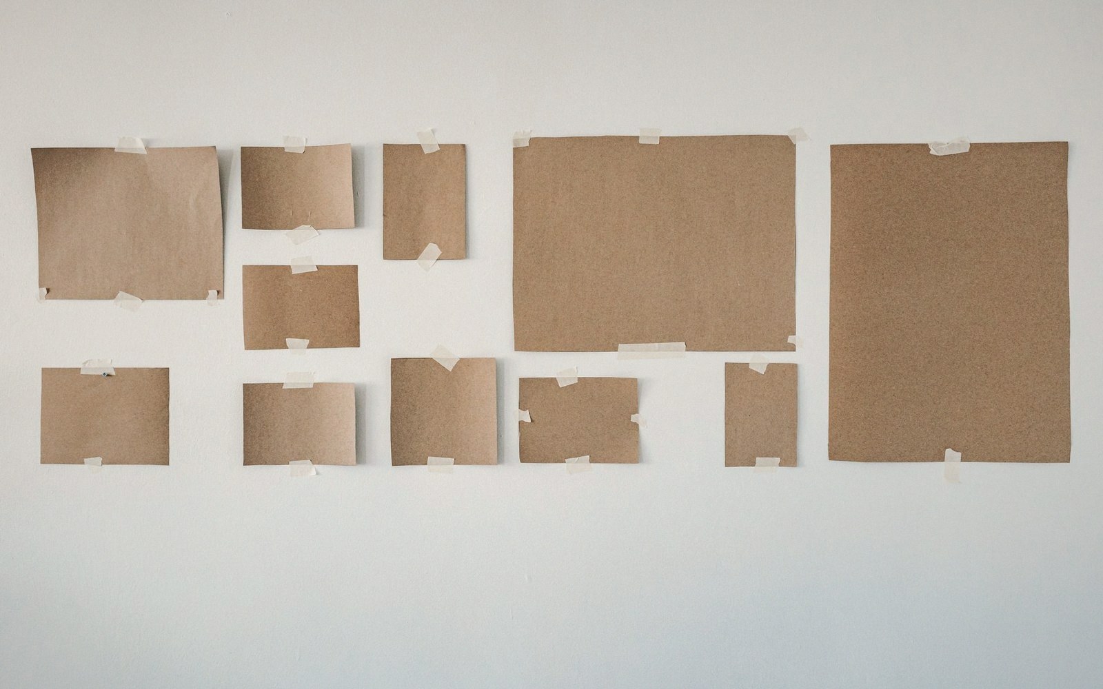 Various sizes of brown paper sheets taped to a white wall in a grid arrangement