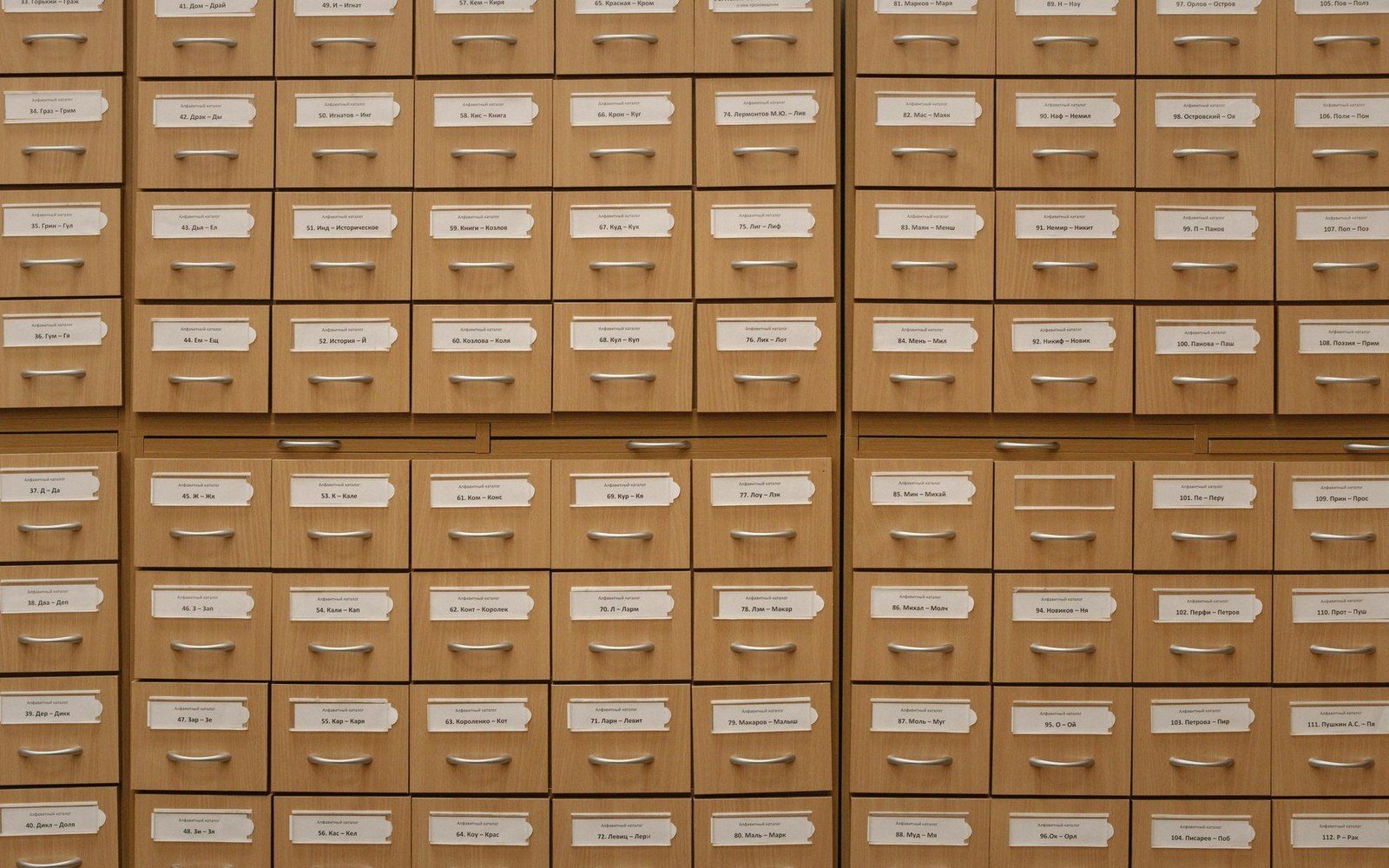 Rows of wooden card catalog drawers with labeled paper tags and metal handles