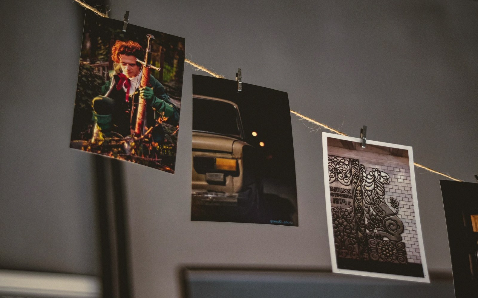 Photo prints clipped to a string, showing a portrait, a car, and a mosaic wall