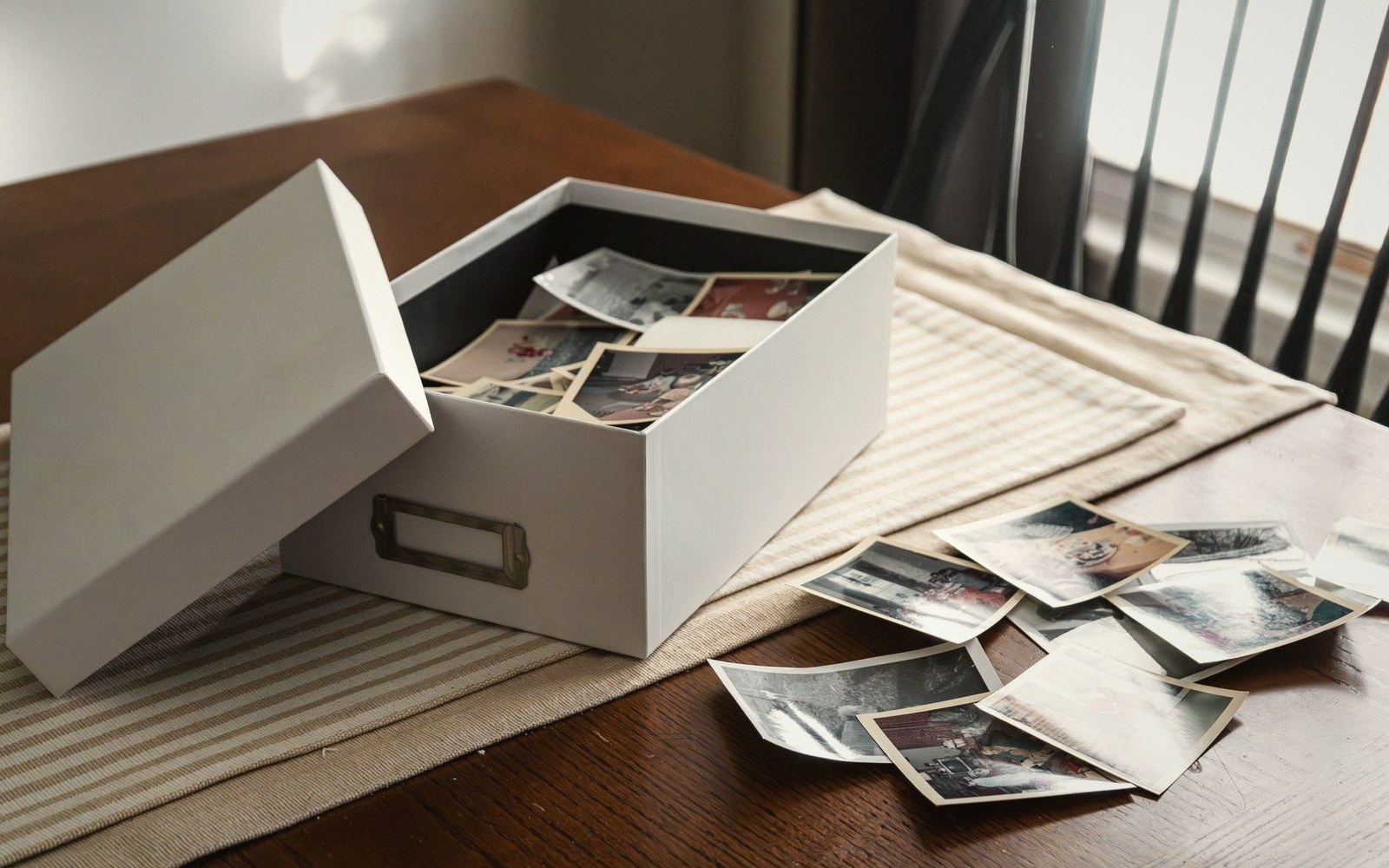 Old photographs spilling out of an open storage box onto a wooden table