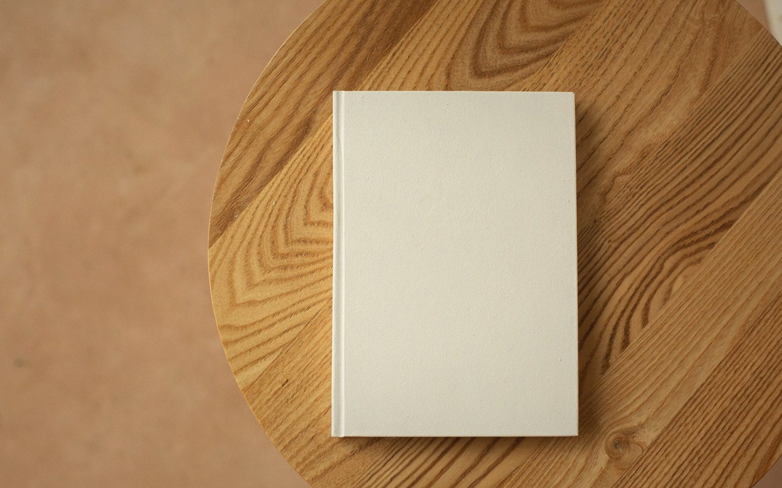 Blank hardcover book mock-up lying on a round wooden table