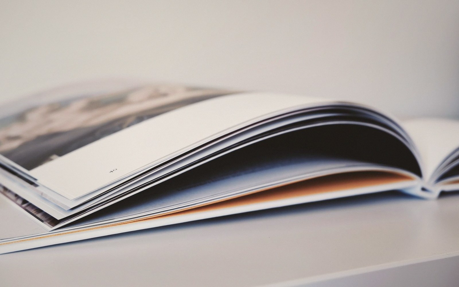 An open photo book with glossy pages curving upward on a white surface