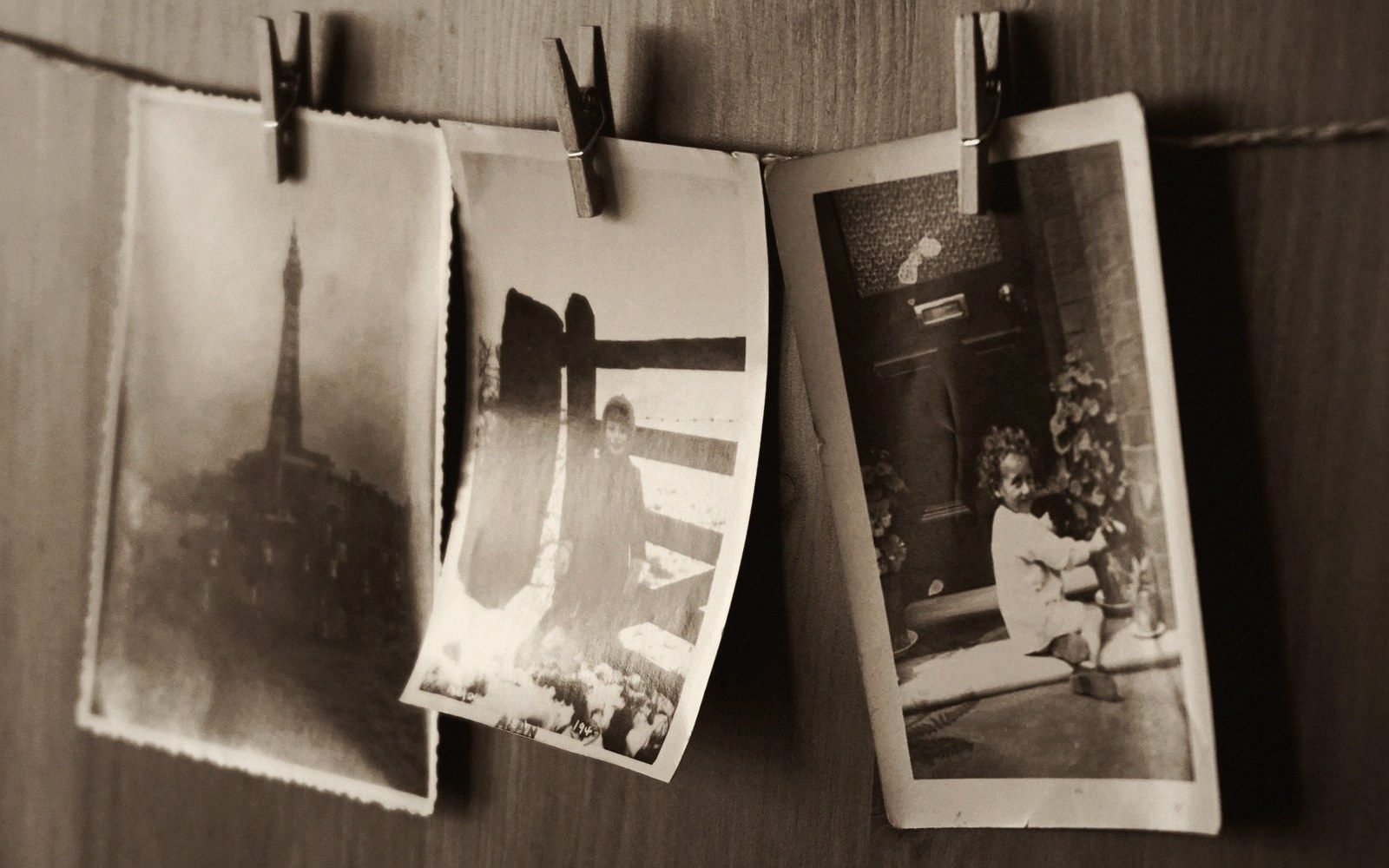 Three sepia-toned vintage photographs pegged to a string against a wooden wall
