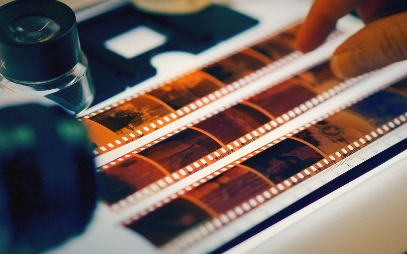 Contact sheets and a loupe on a light table with hands sorting